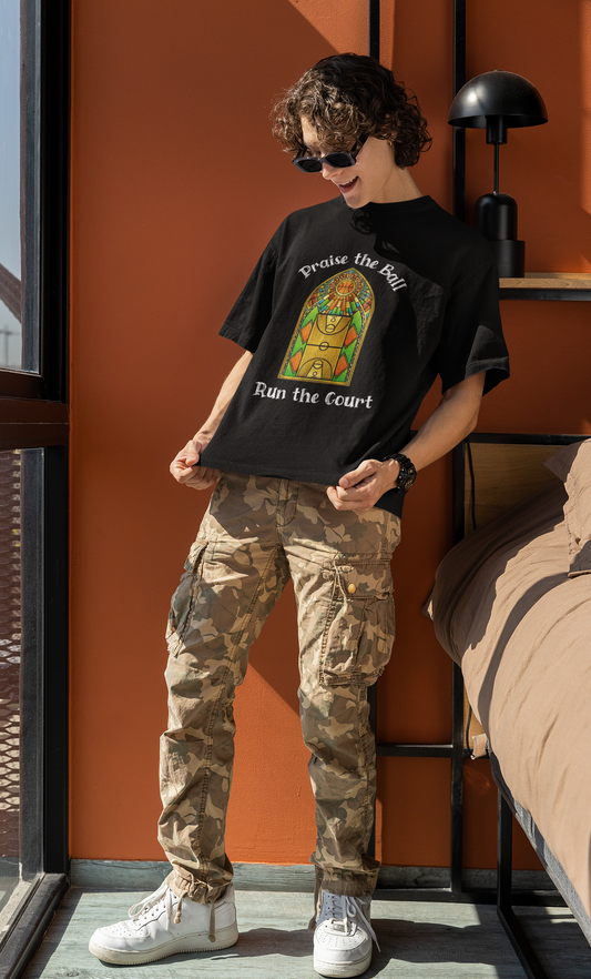 Mockup mit Model Schwarzes Oversized Basketball T-Shirt mit einem Print im Stil eines Kirchen-Buntglasfensters, der einen Basketball-Court zeigt. Darüber steht „Praise the Ball“ und darunter „Run the Court“ in einer gotischen Schriftart. 100% Baumwolle