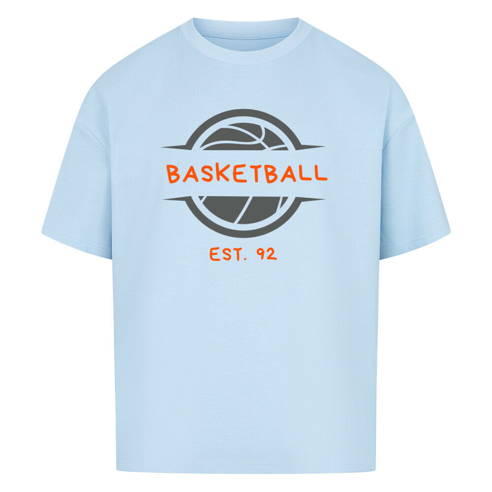 Babyblaues Oversized T-Shirt mit einem Print eines grauen Basketball-Emblems und dem orangefarbenen, stilisierten Text „BASKETBALL“ und „EST. 92“. 100% Baumwolle.