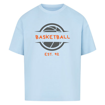 Babyblaues Oversized T-Shirt mit einem Print eines grauen Basketball-Emblems und dem orangefarbenen, stilisierten Text „BASKETBALL“ und „EST. 92“. 100% Baumwolle.