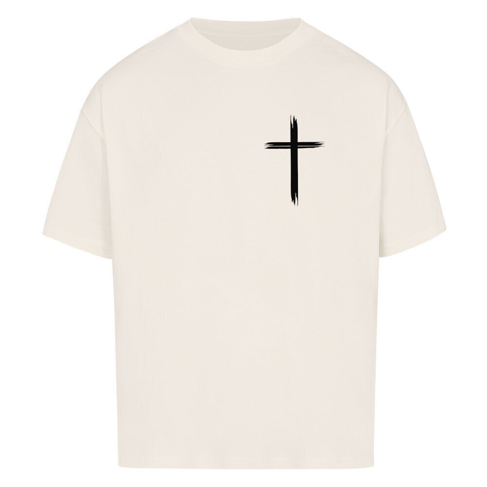 Vorderseite eines natural raw Oversized T-Shirts mit einem kleinen, schwarzen, stilisierten Pinselstrich-Kreuz auf der linken Brust. 100% Baumwolle