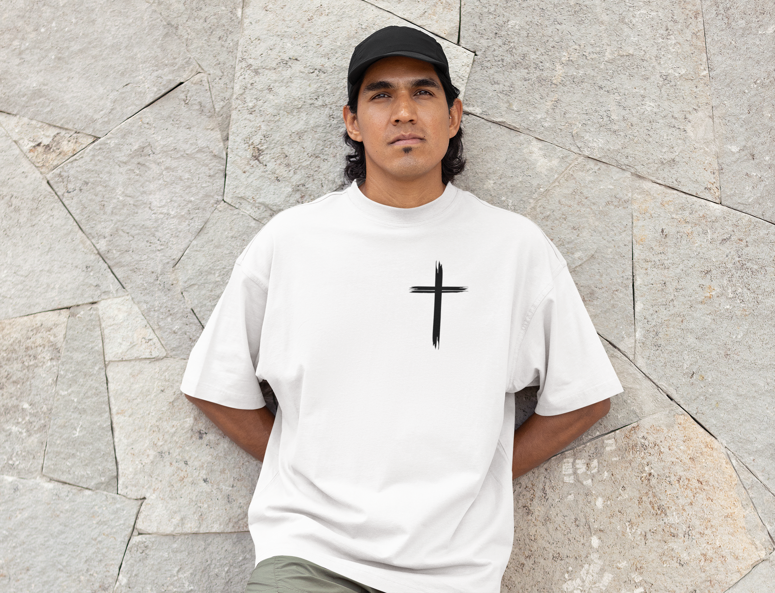 Vorderseite eines mockupit Model im weißen Oversized T-Shirts mit einem kleinen, schwarzen, stilisierten Pinselstrich-Kreuz auf der linken Brust. 100% Baumwolle