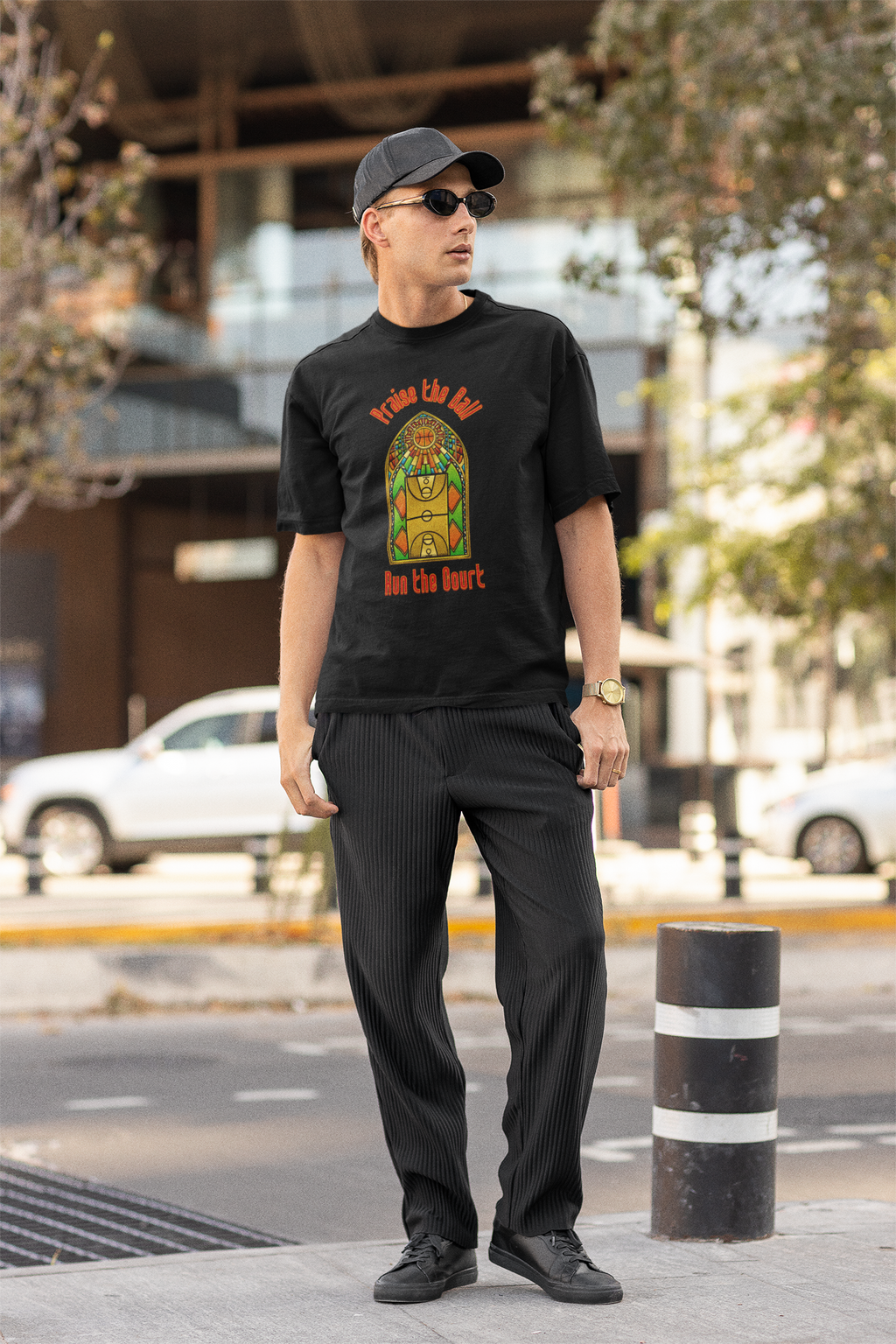 Mockup mit Model Schwarzes Oversized T-Shirt mit einem Print im Stil eines Kirchen-Buntglasfensters, der einen Basketball-Court zeigt. Darüber steht in Rot „Praise the Ball“ und darunter „Run the Court“. 100% Baumwolle.