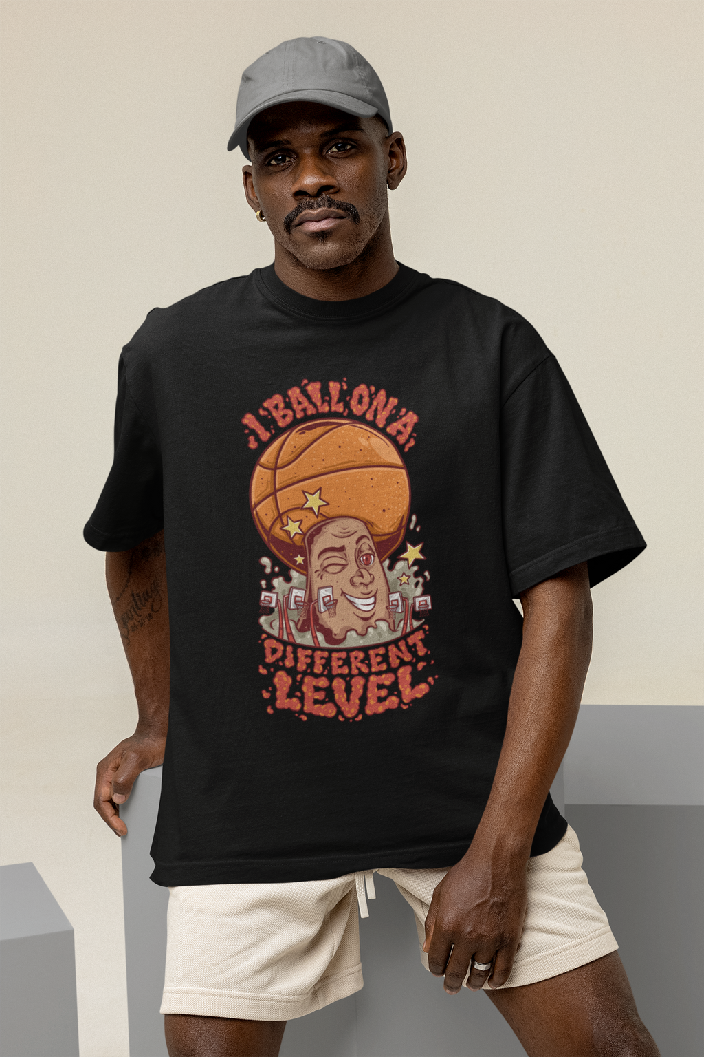 Mockup mit Model Schwarzes Oversized Basketball T-Shirt mit einem bunten Cartoon-Print einer zwinkernden Figur, die einen Basketball als Kopf hat. Der rote Text lautet „I BALL ON A DIFFERENT LEVEL“. 100% Baumwolle