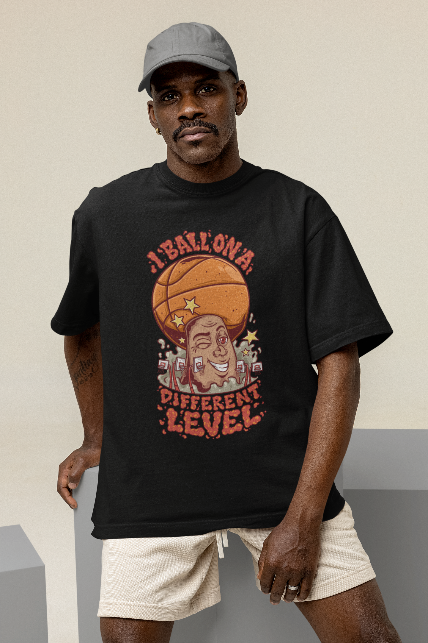 Mockup mit Model Schwarzes Oversized Basketball T-Shirt mit einem bunten Cartoon-Print einer zwinkernden Figur, die einen Basketball als Kopf hat. Der rote Text lautet „I BALL ON A DIFFERENT LEVEL“. 100% Baumwolle