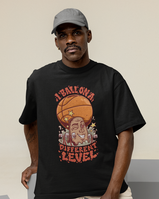 Mockup mit Model Schwarzes Oversized Basketball T-Shirt mit einem bunten Cartoon-Print einer zwinkernden Figur, die einen Basketball als Kopf hat. Der rote Text lautet „I BALL ON A DIFFERENT LEVEL“. 100% Baumwolle