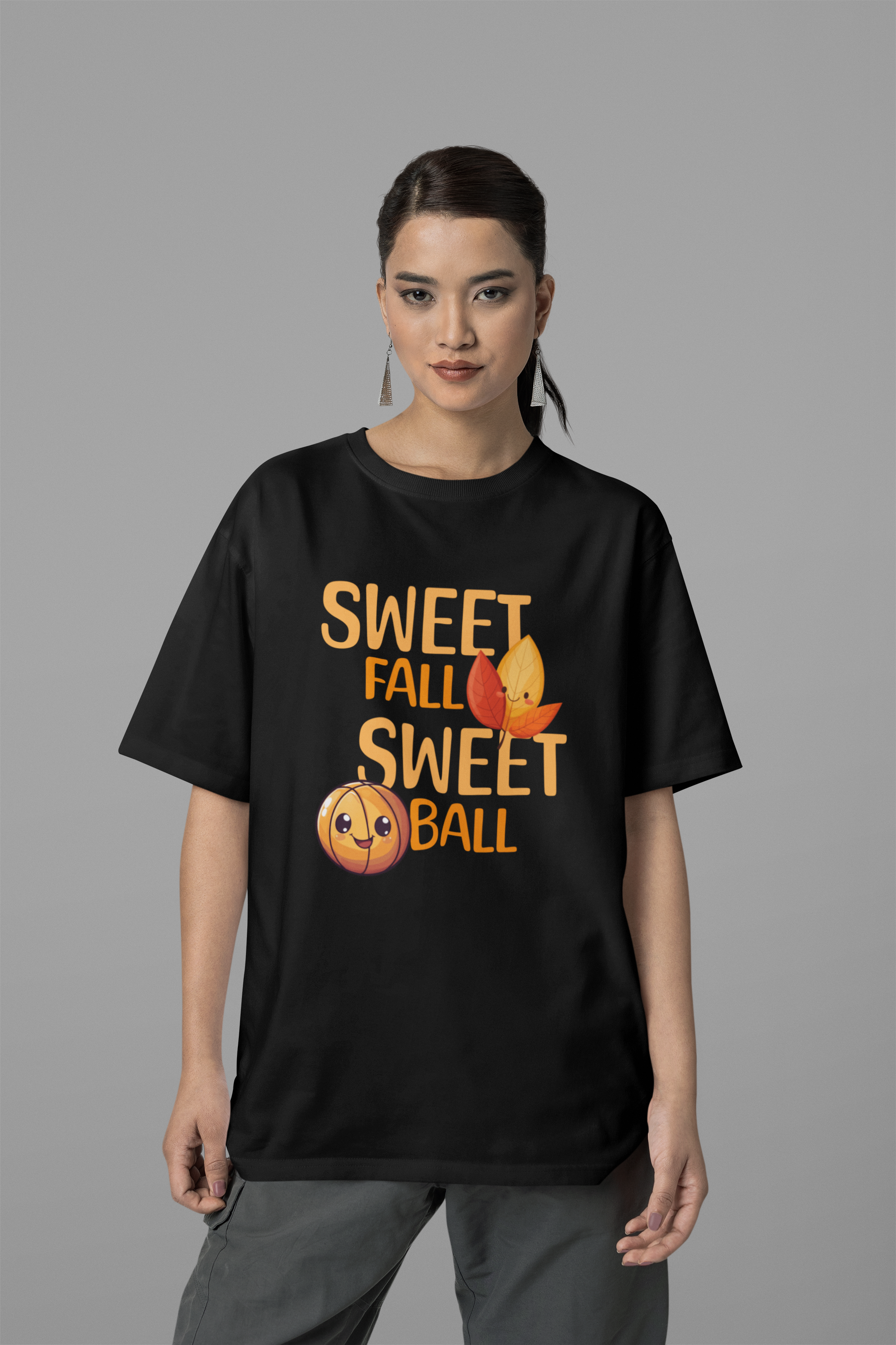 Mockup mit Schwarzen Oversized T-Shirt mit orangefarbenem Print „SWEET FALL SWEET BALL“, verziert mit einem niedlichen lächelnden Basketball und zwei lachenden Herbstblättern – 100% Baumwolle.