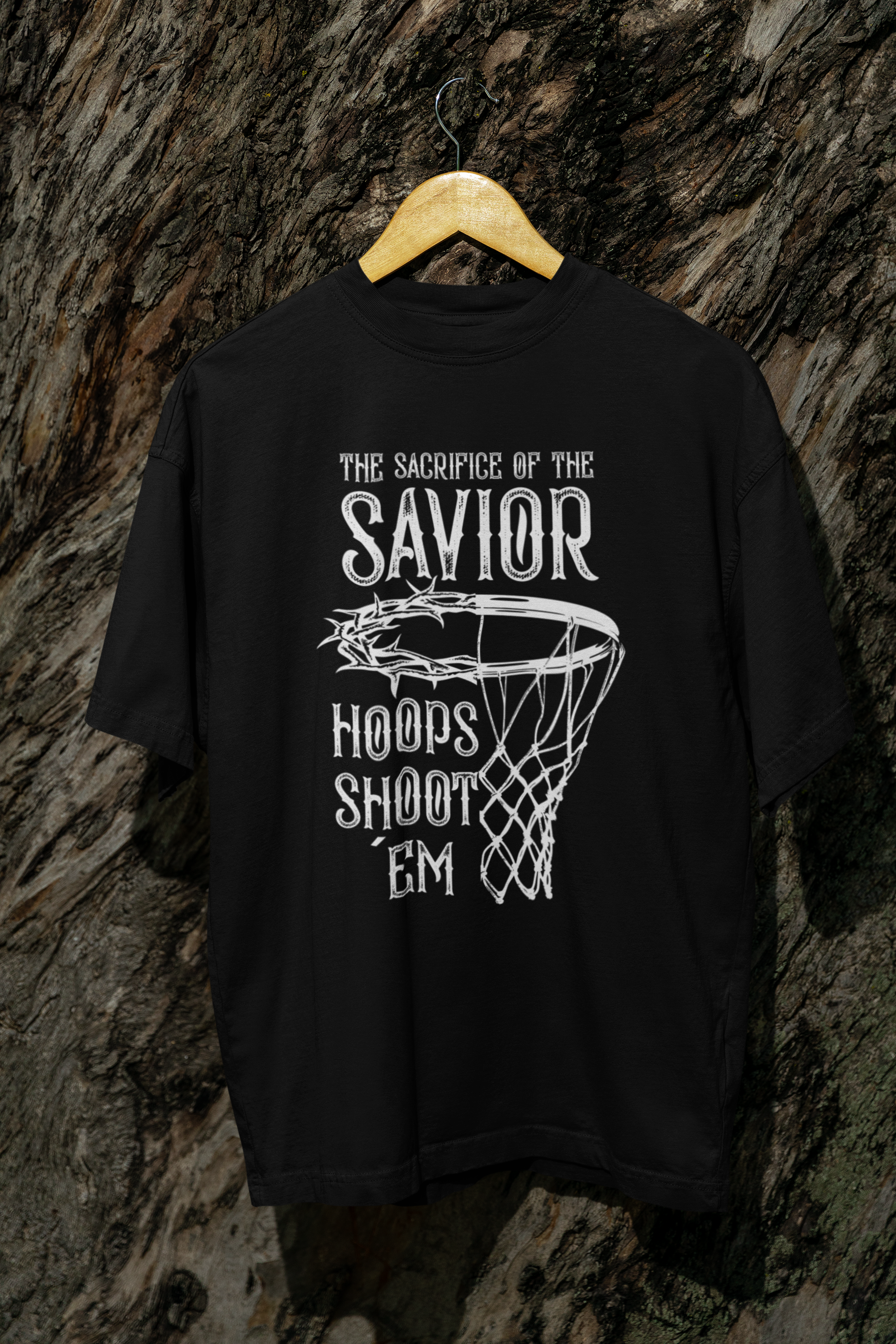 Mockup Schwarzes Oversized T-Shirt mit einem weißen Print, der einen Basketballkorb zeigt, dessen Ring eine Dornenkrone ist. Darüber steht der Text „THE SACRIFICE OF THE SAVIOR“ und darunter „HOOPS SHOOT EM“. 100% Baumwolle.