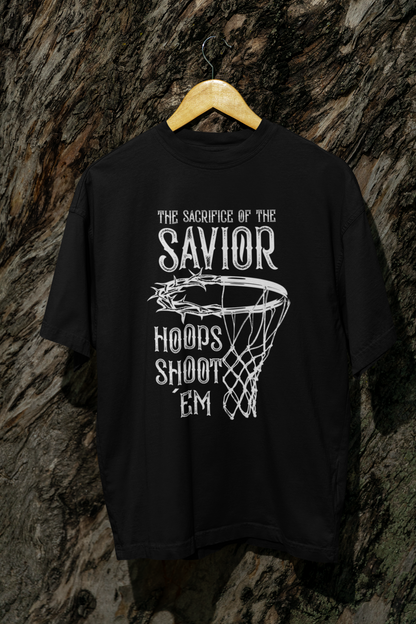 Mockup Schwarzes Oversized T-Shirt mit einem weißen Print, der einen Basketballkorb zeigt, dessen Ring eine Dornenkrone ist. Darüber steht der Text „THE SACRIFICE OF THE SAVIOR“ und darunter „HOOPS SHOOT EM“. 100% Baumwolle.