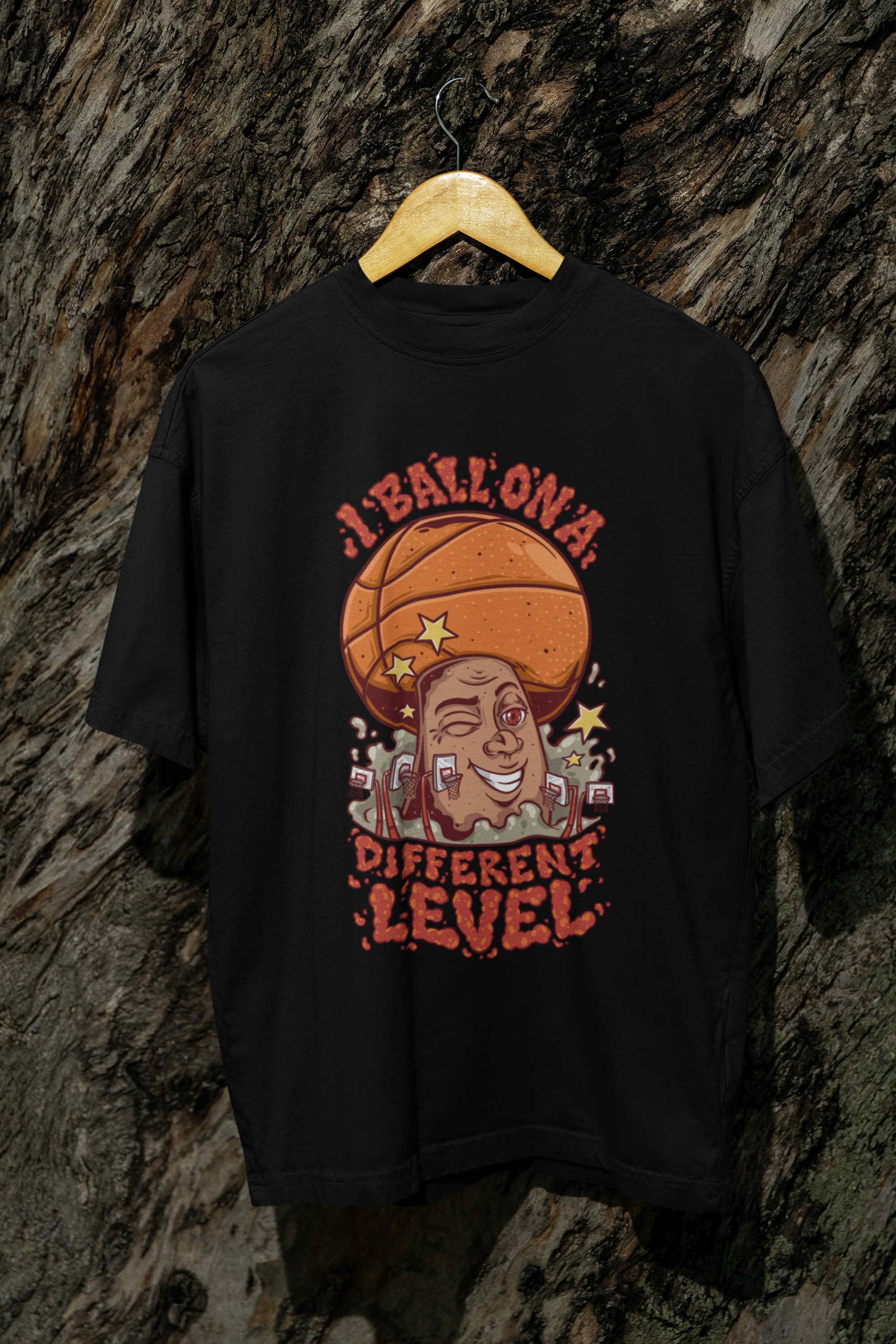 Mockup Schwarzes Oversized Basketball T-Shirt mit einem bunten Cartoon-Print einer zwinkernden Figur, die einen Basketball als Kopf hat. Der rote Text lautet „I BALL ON A DIFFERENT LEVEL“. 100% Baumwolle