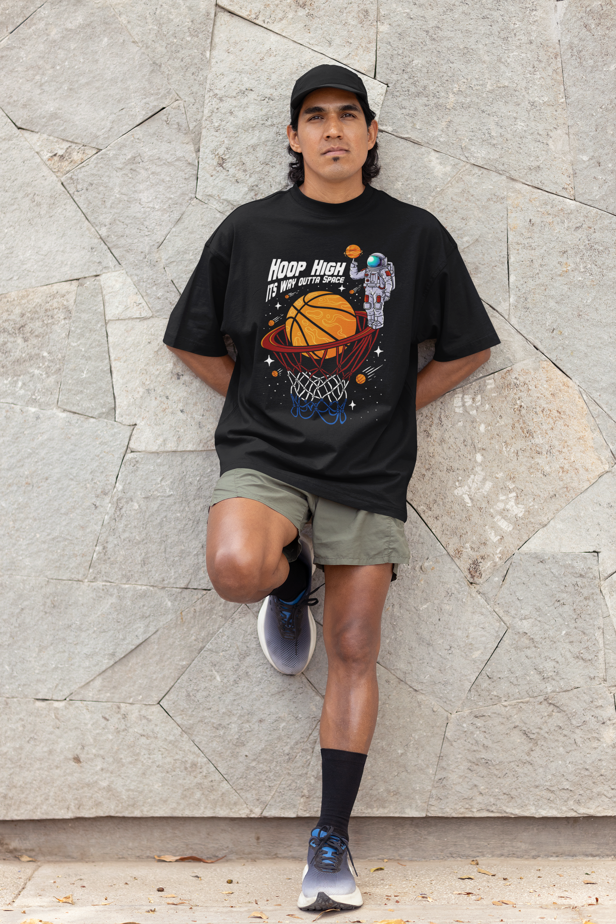 Mockup mit Model Schwarzes Oversized T-Shirt mit einem bunten Print eines Astronauten im Weltall, der einen Basketball in einen Korb dunkt. Der Slogan lautet: "HOOP HIGH ITS WAY OUTTA SPACE". 100% Baumwolle.