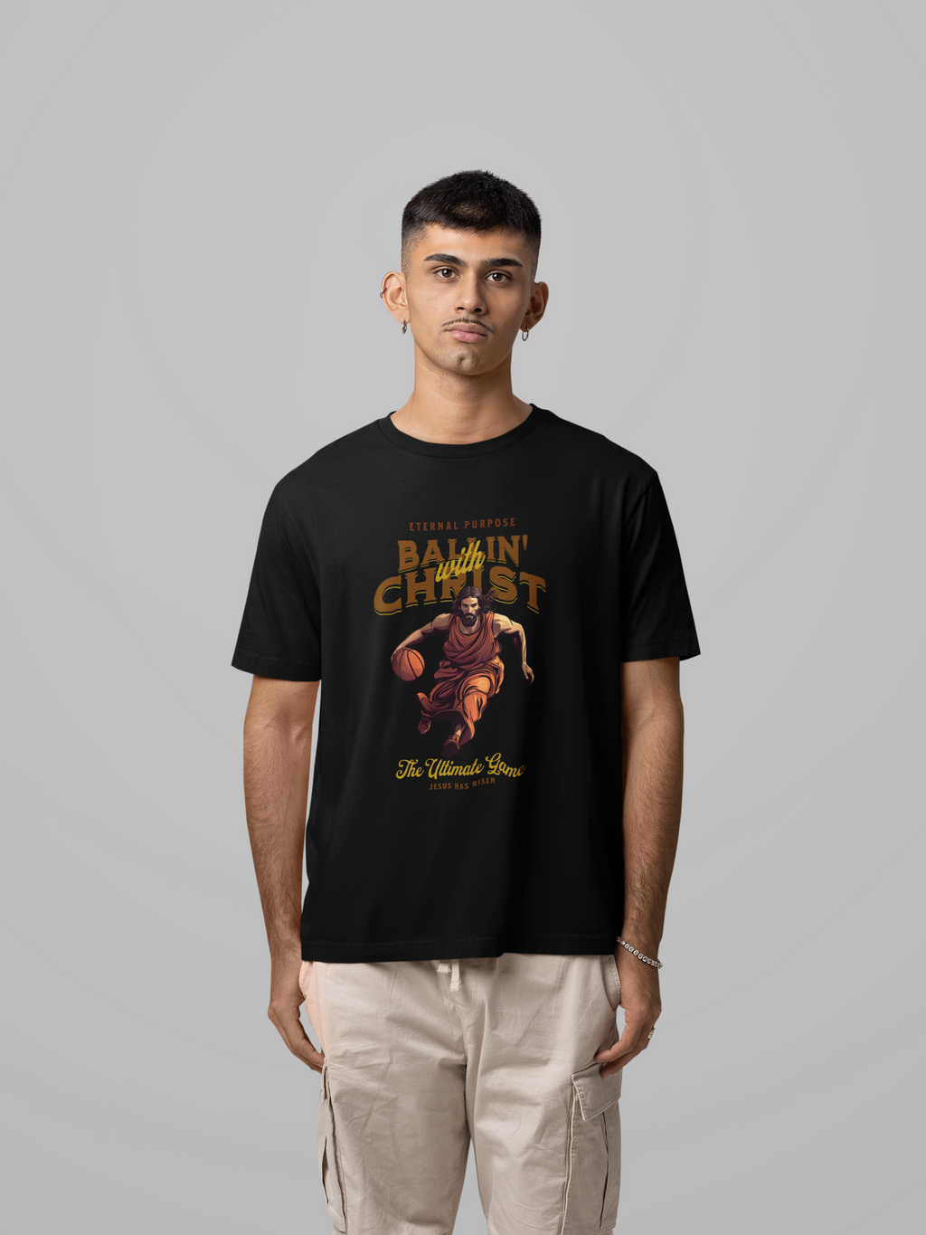 Mockup mit Mann Schwarzes Oversize T-Shirt aus 100% Baumwolle mit einem braun-gelben Vintage-Print. Das Motiv zeigt Jesus Christus in Robe, wie er einen Basketball dribbelt. Der Text lautet "ETERNAL PURPOSE BALLIN´ WITH CHRIST THE ULTIMATE GAME". 