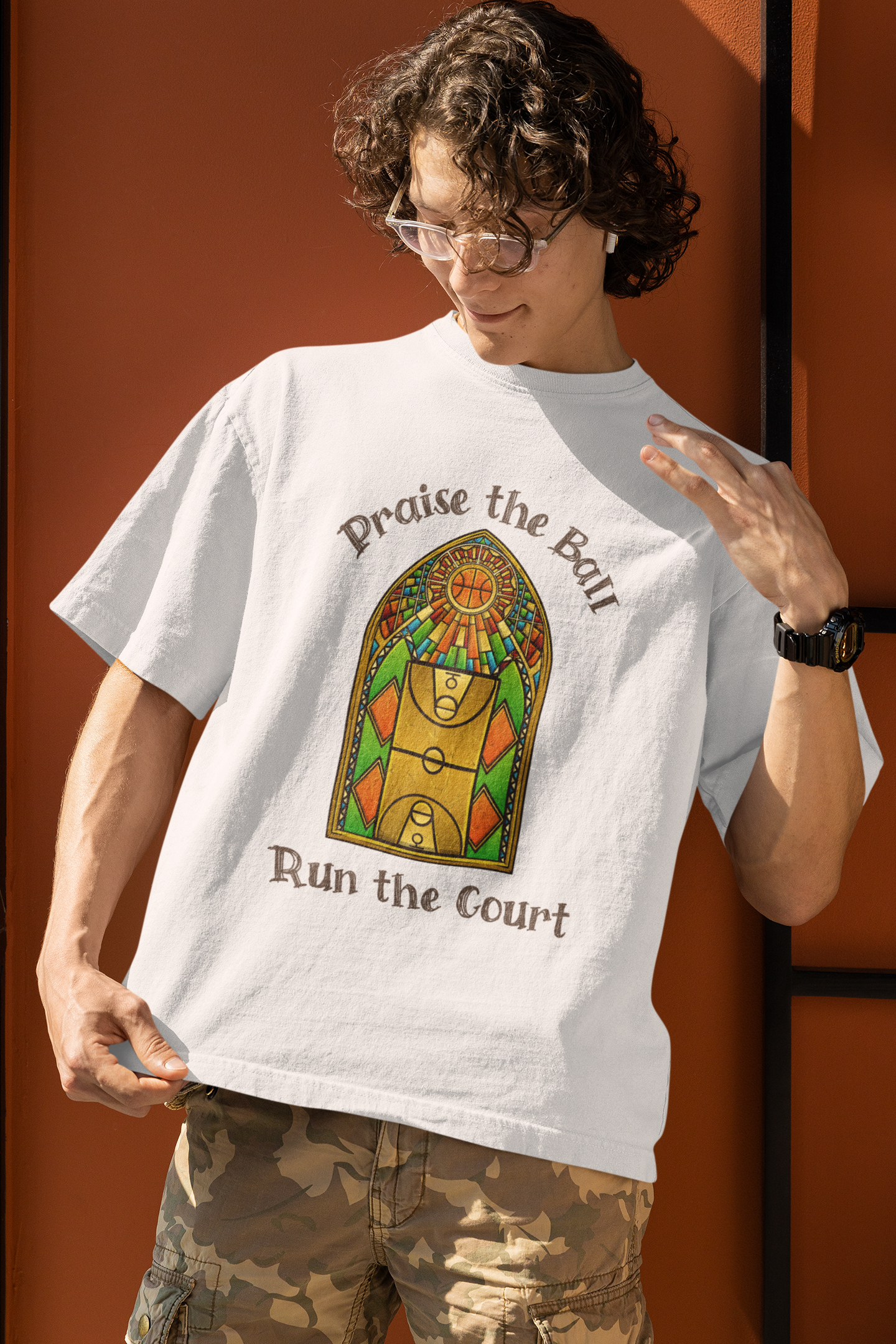 Mockup mit Model Weißes Oversized Basketball T-Shirt mit einem Print im Stil eines Kirchen-Buntglasfensters, der einen Basketball-Court zeigt. Darüber steht „Praise the Ball“ und darunter „Run the Court“ in einer gotischen Schriftart. 100% Baumwolle 