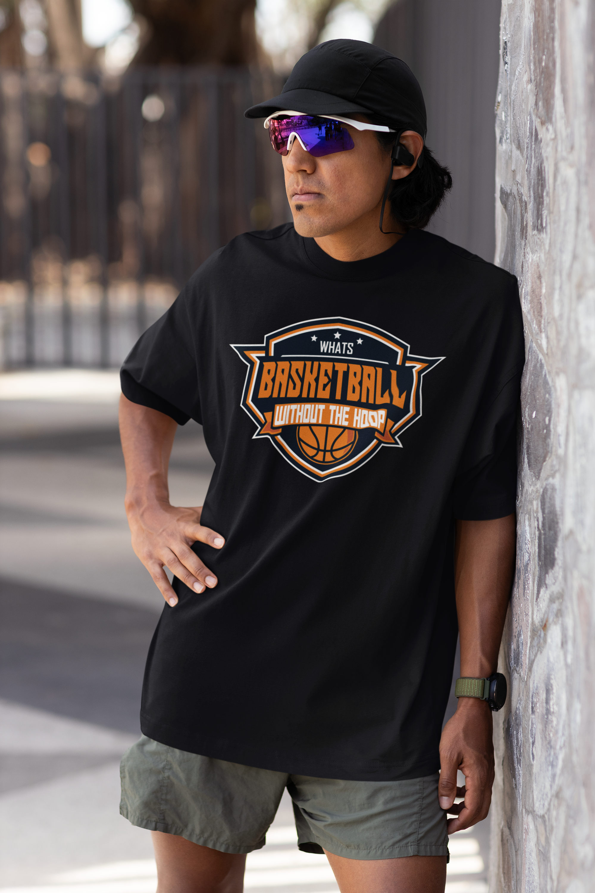 Mockup mit Model Schwarzes Oversized T-Shirt mit einem Basketball-Logo im Wappen-Stil in Orange, Weiß und Blau und dem Slogan "WHAT'S BASKETBALL WITHOUT THE HOOP". 100% Baumwolle.