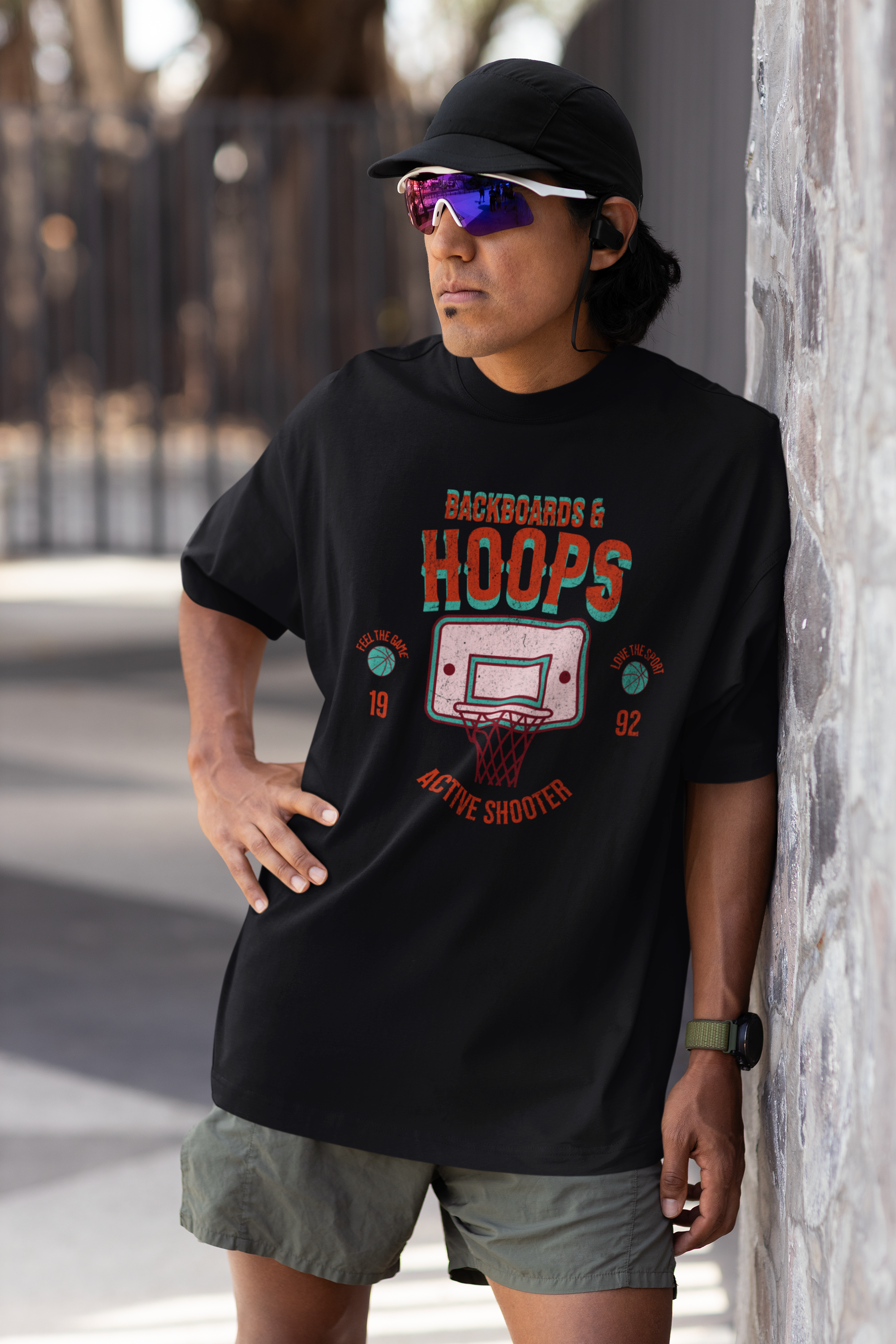 Mockup mit Model Schwarzes Oversized T-Shirt mit 90er-Jahre-Retro-Print eines Basketballkorbs und den Schriftzügen „BACKBOARDS & HOOPS“, „ACTIVE SHOOTER“ und „19 92“ in Orange und Türkis. 100% Baumwolle.