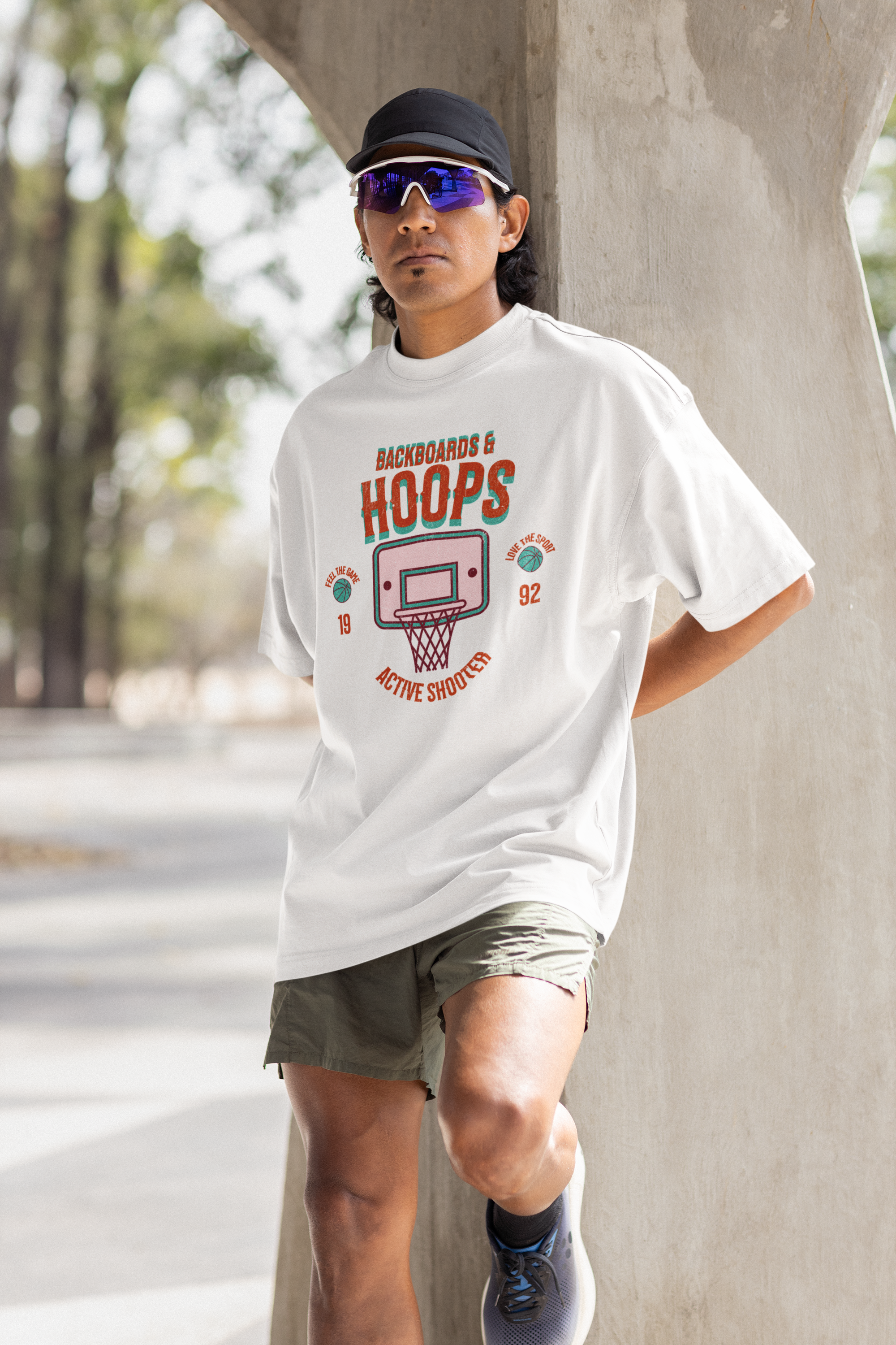 Mockupit Model Weißes Oversized T-Shirt mit 90er-Jahre-Retro-Print eines Basketballkorbs und den Schriftzügen „BACKBOARDS & HOOPS“, „ACTIVE SHOOTER“ und „19 92“ in Orange und Türkis. 100% Baumwolle.