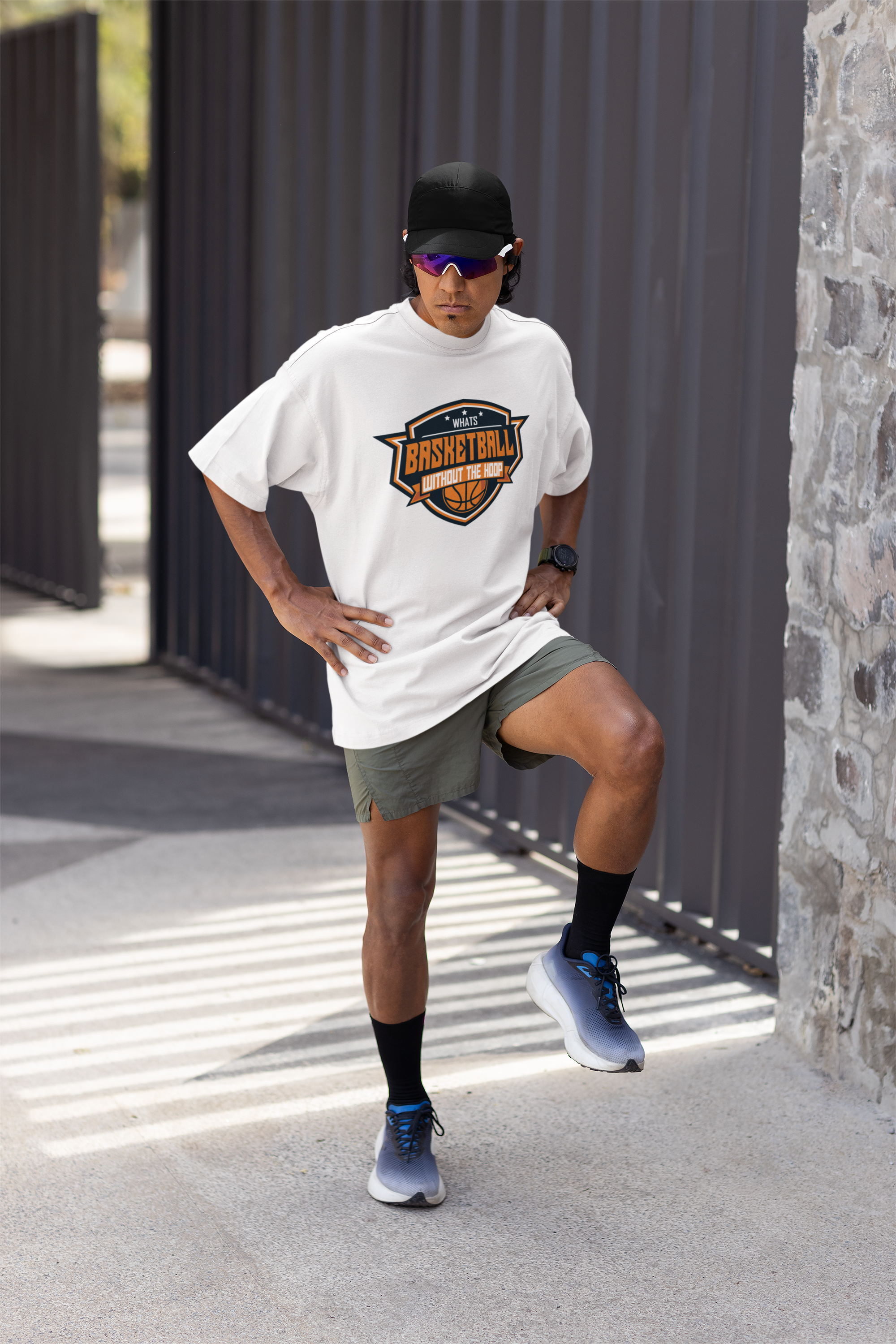 Mockup mit Model Weißes Oversized T-Shirt mit einem Basketball-Logo im Wappen-Stil in Orange, Weiß und Blau und dem Slogan "WHAT'S BASKETBALL WITHOUT THE HOOP". 100% Baumwolle.