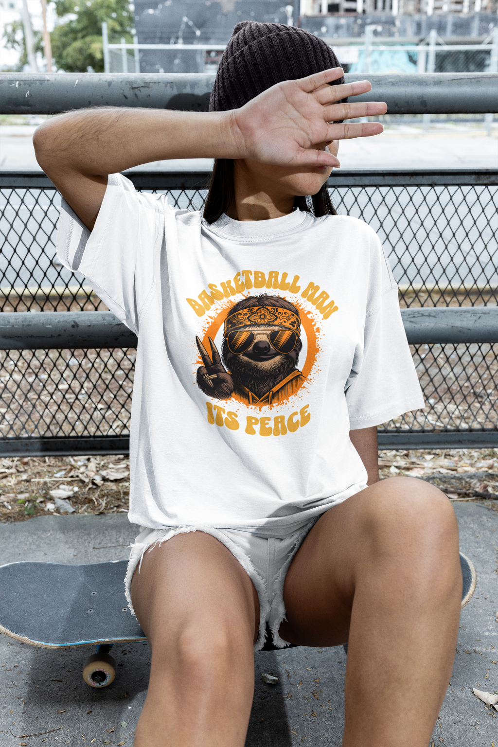 Mockupit Model Weißes Oversized Basketball T-Shirt mit einem 70er-Jahre-Retro-Print eines coolen Faultiers (Sloth) mit Sonnenbrille und Bandana, das ein Peace-Zeichen macht. Der Text lautet „BASKETBALL MAN“ und „ITS PEACE“ in Orange und Gelb. 100% Baumwolle.