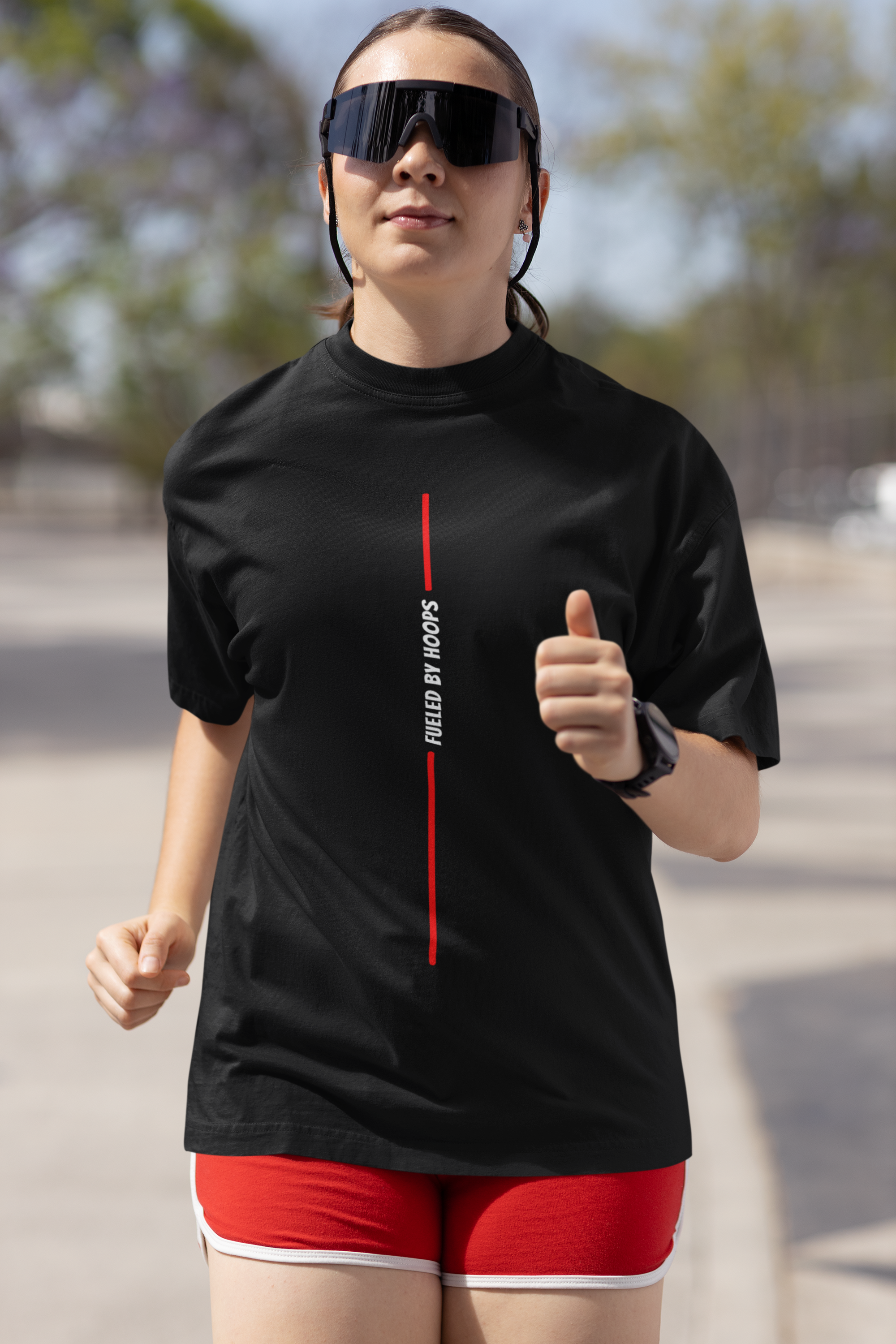 Mockup mit Model Schwarzes Oversized T-Shirt mit einem minimalistischen, vertikalen Print: Eine rote Linie wird in der Mitte vom vertikalen, weißen Text „FUELED BY HOOPS“ unterbrochen. 100% Baumwolle.